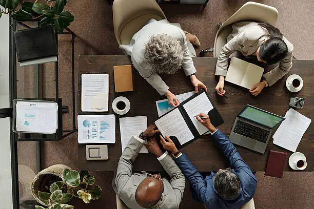 Team reviewing documents and a laptop around a meeting table, seen from above
